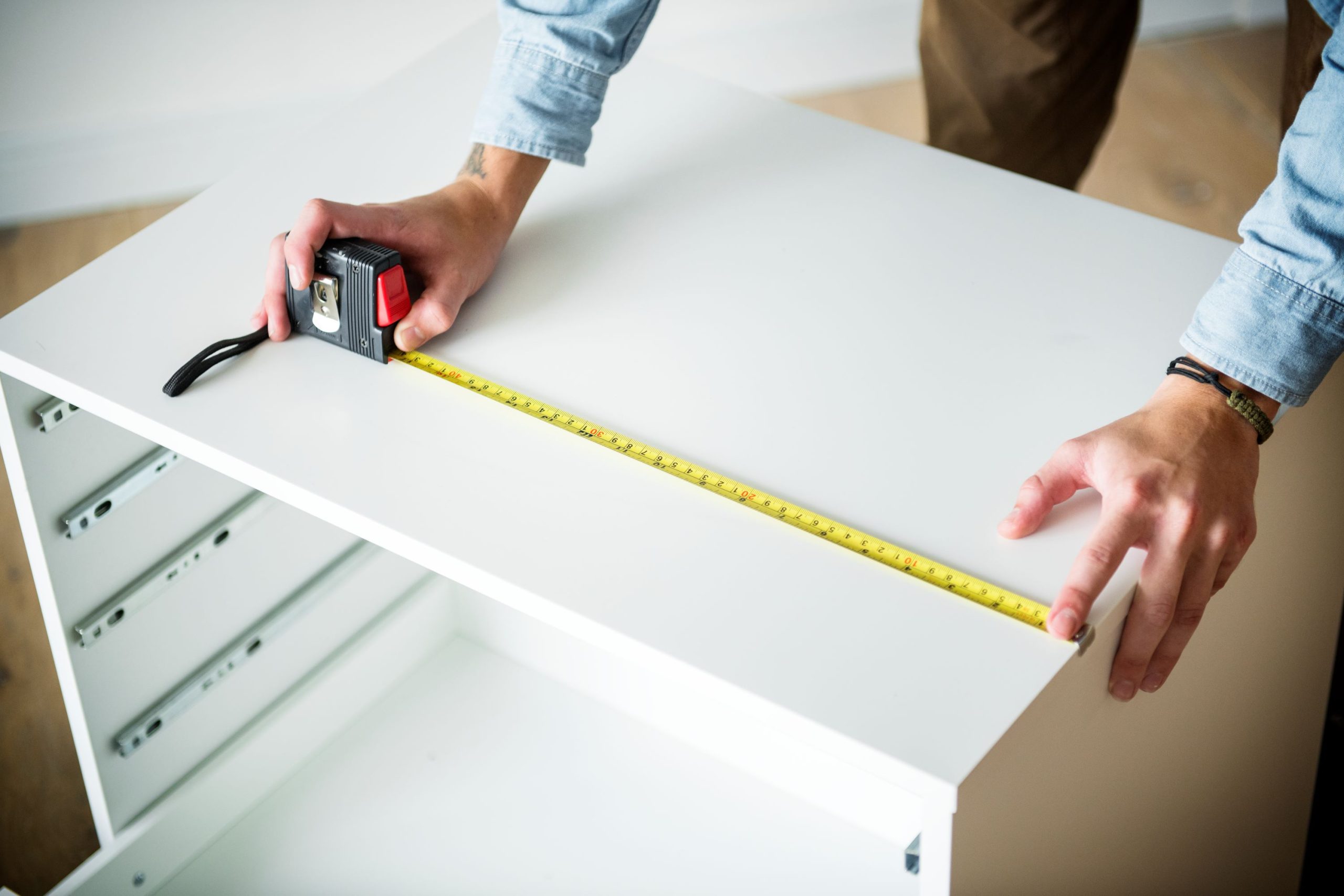 person-measuring-white-furniture-with-a-yellow-tap-2026-03-18-11-49-57-utc